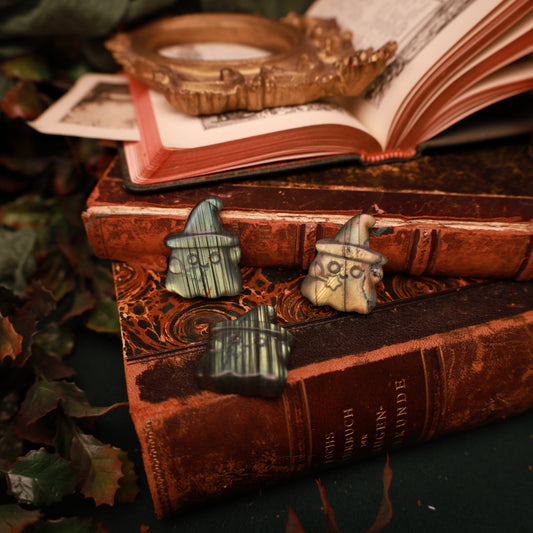 Drei Labradorit-Geister mit spitzen Hüten auf alten Büchern, zwei von vorn mit Gesicht und Stern-Zauberstab, einer mit der Rückseite sichtbar.
