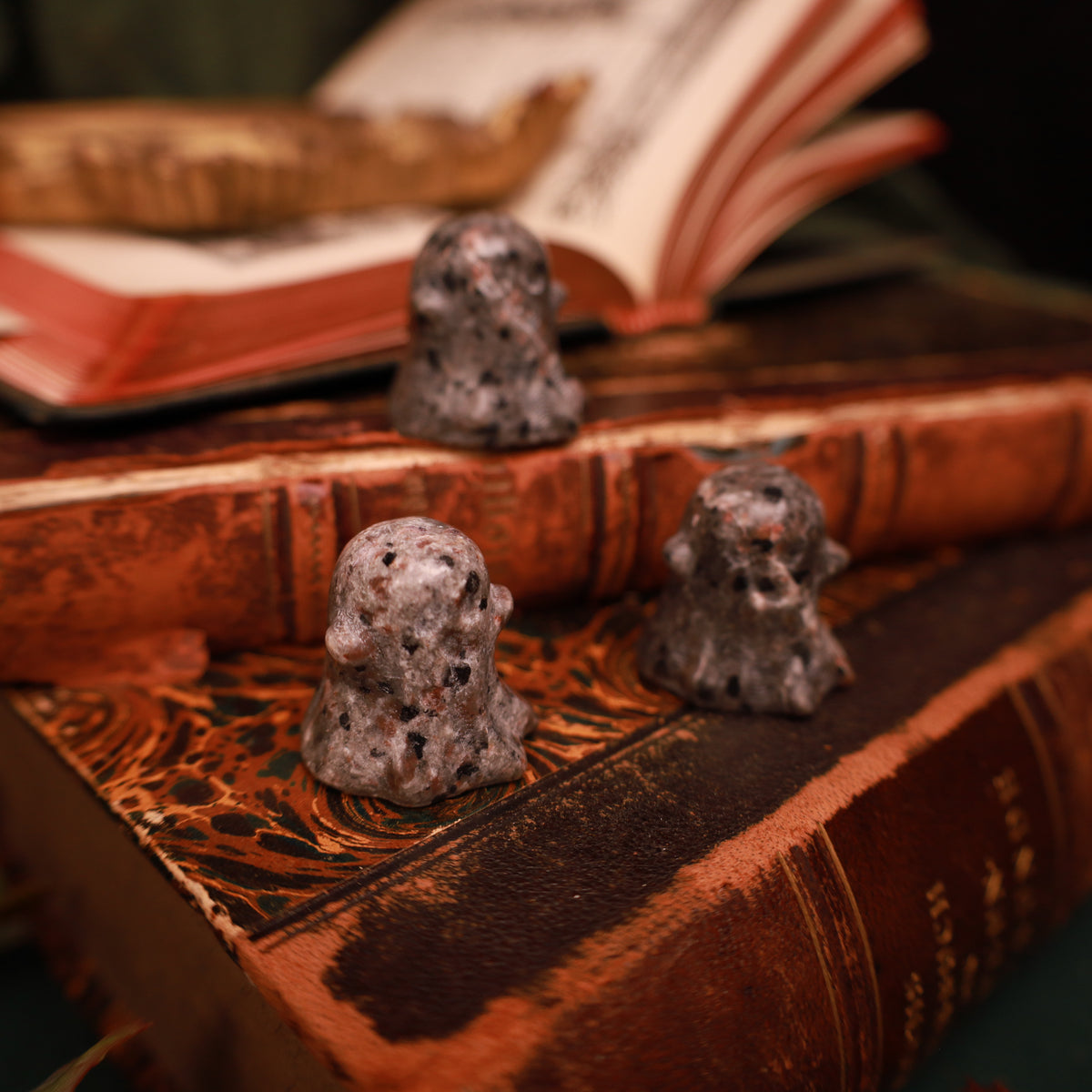 Drei kleine Yooperlite-Geister mit gerundeten Köpfen, seitlichen Armen und grau-bräunlicher, dunkel gesprenkelter Steinzeichnung auf alten Büchern.